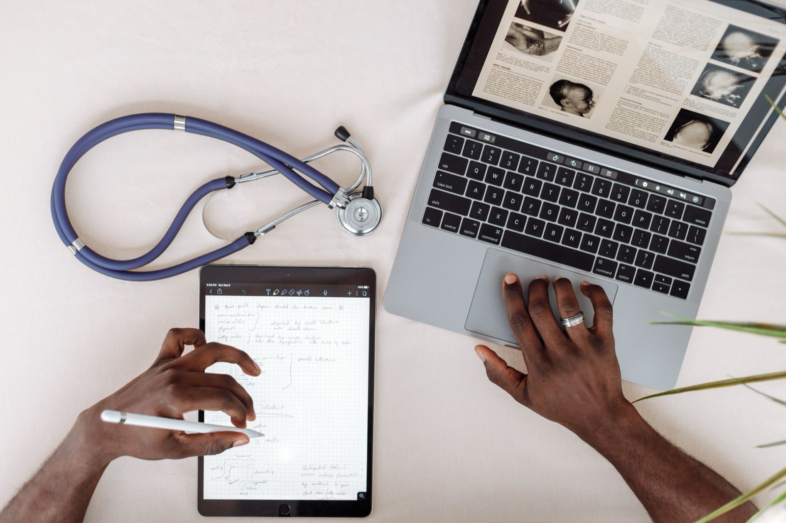 A medical professional working across a tablet and laptop next to a stethoscope