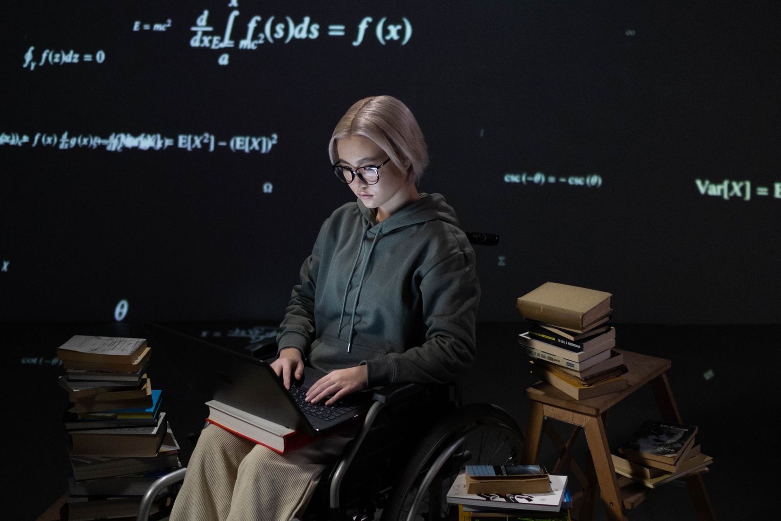 A student in a wheelchair studying on a laptop surrounded by books