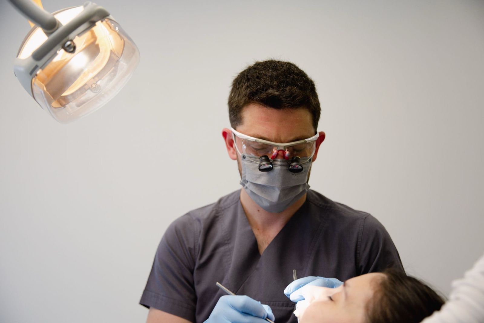 A dentist examining a patient under an exam light in a dental office