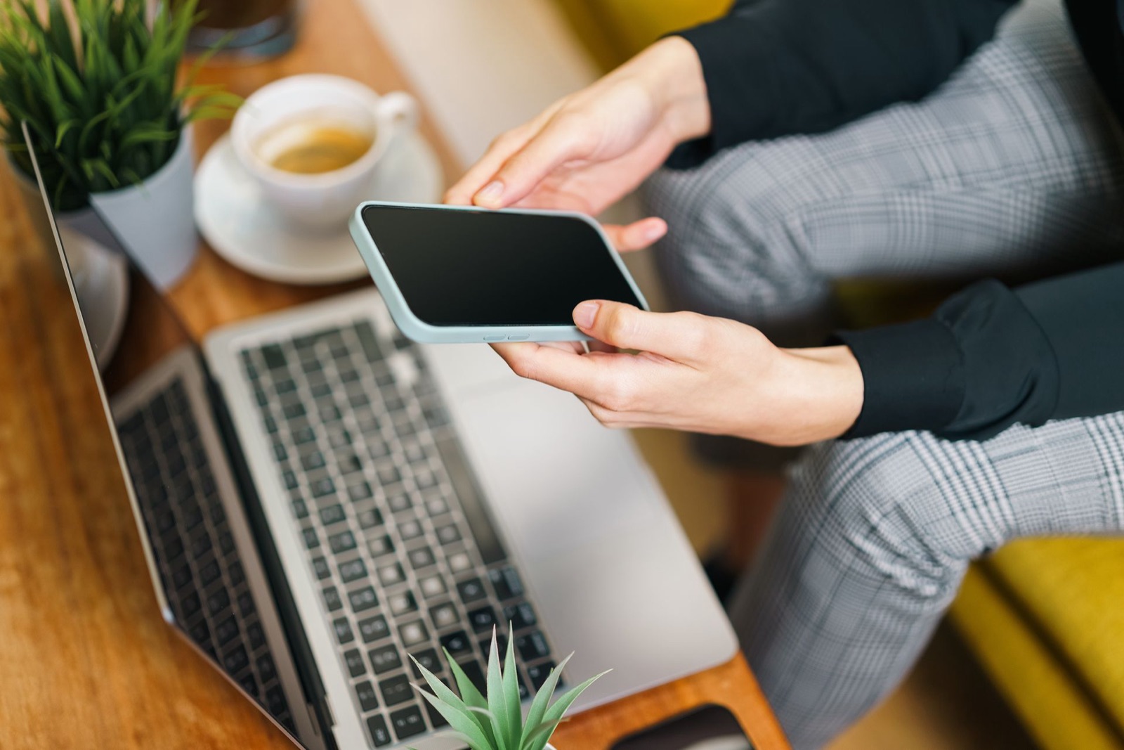 A marketer holding a smartphone above a laptop at an office desk