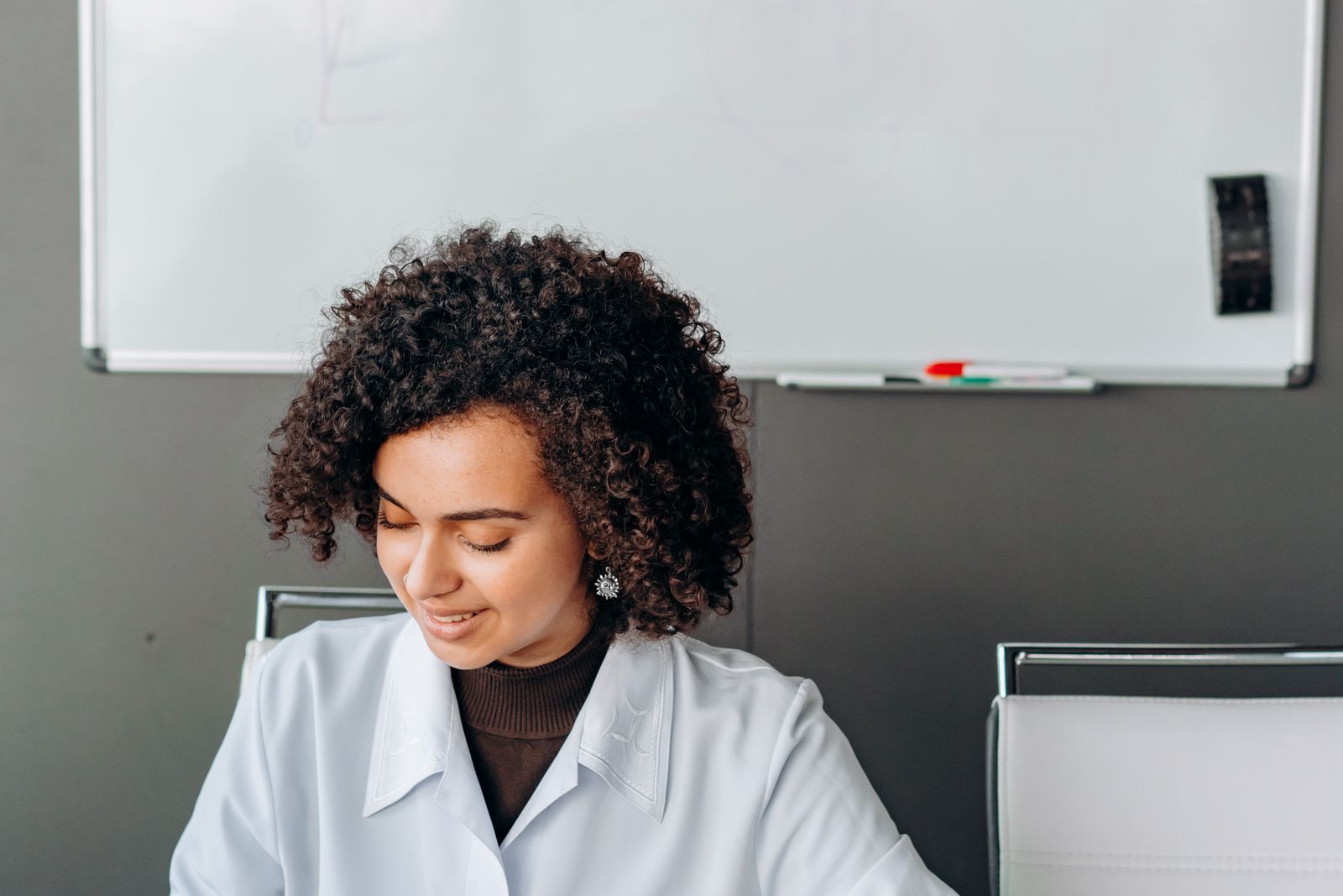 A Woman in White Long Sleeves Writing on Whiteboard