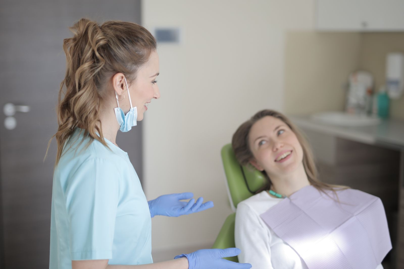 Cheerful young female dentist talking with patient during therapy in modern hospital