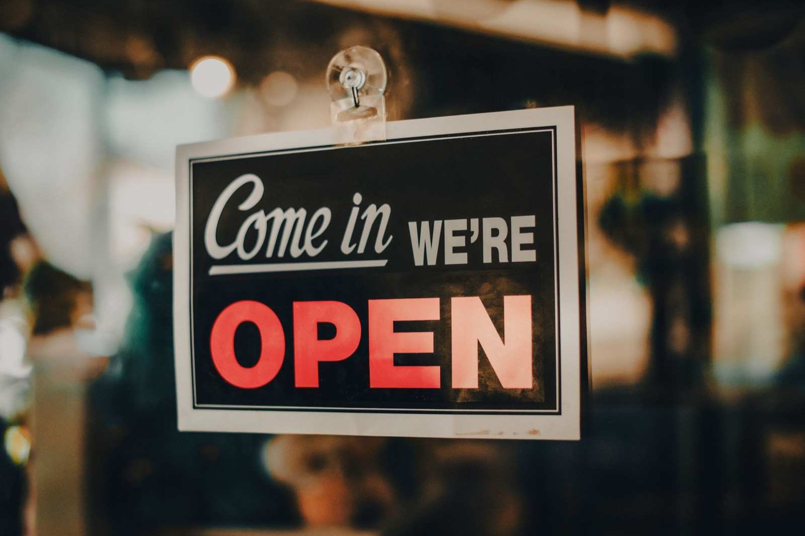 A come in we are open sign hanging in a local shop window