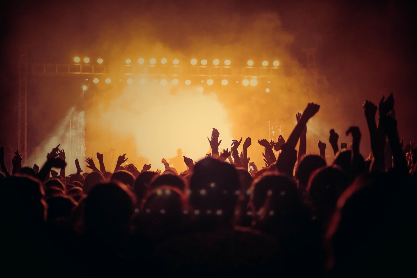 A crowd with raised hands at a concert venue under warm stage lights