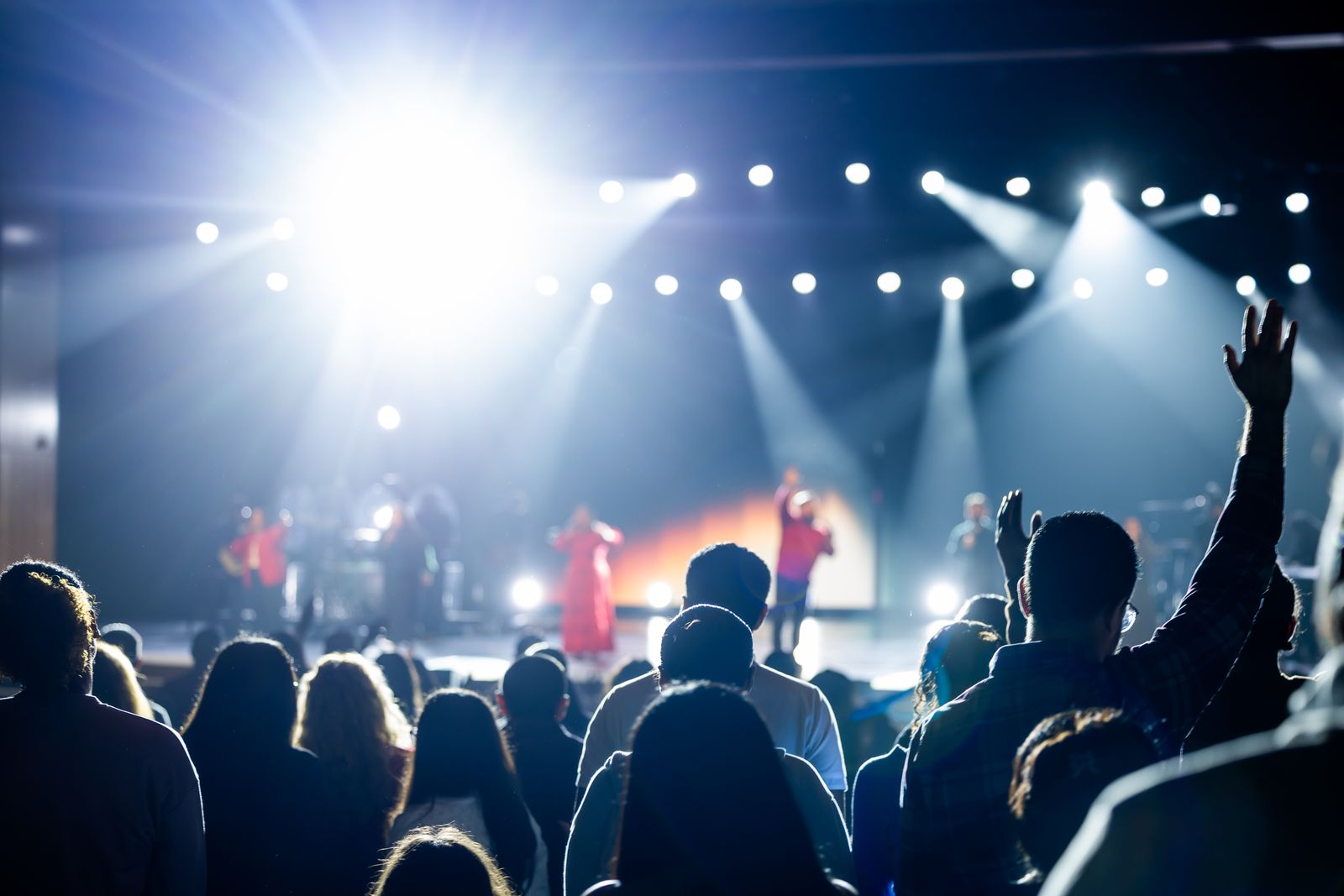 Singer greeting a packed crowd under blue stage lights at a live music venue