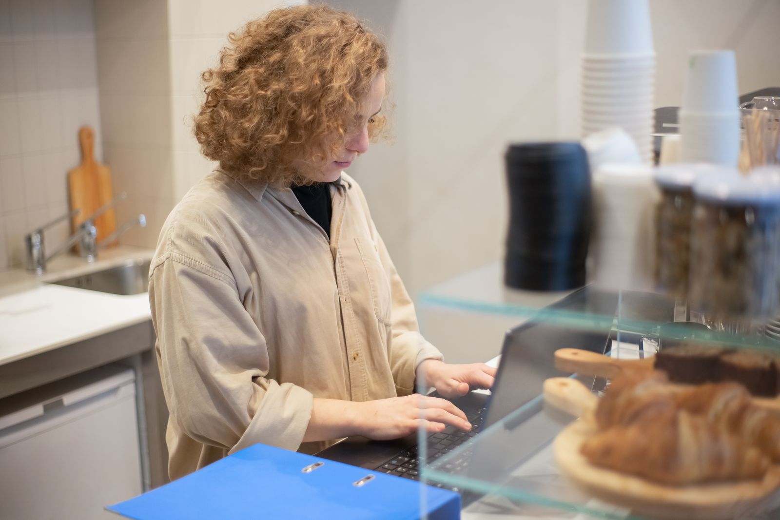 A cafe owner replying to messages on a laptop behind the counter