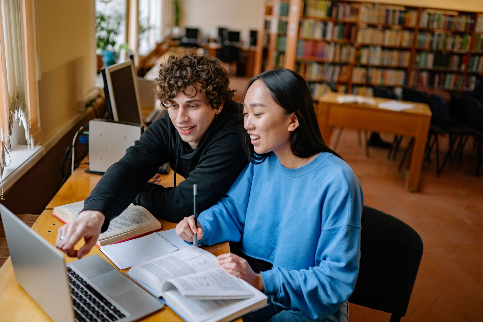Students Studying in a Library Using Laptop and Books