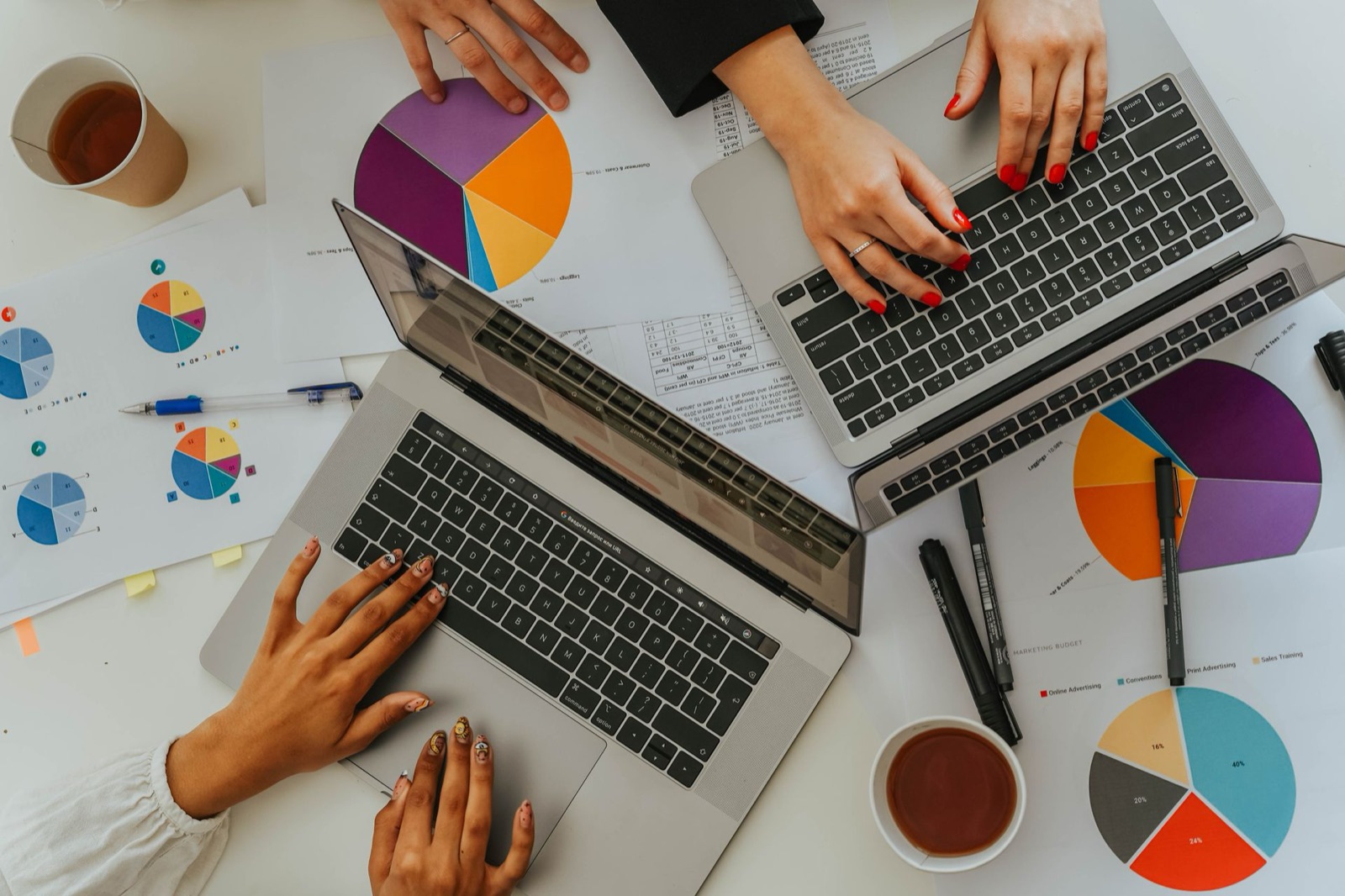 Overhead view of a team comparing pie charts and laptops on a desk