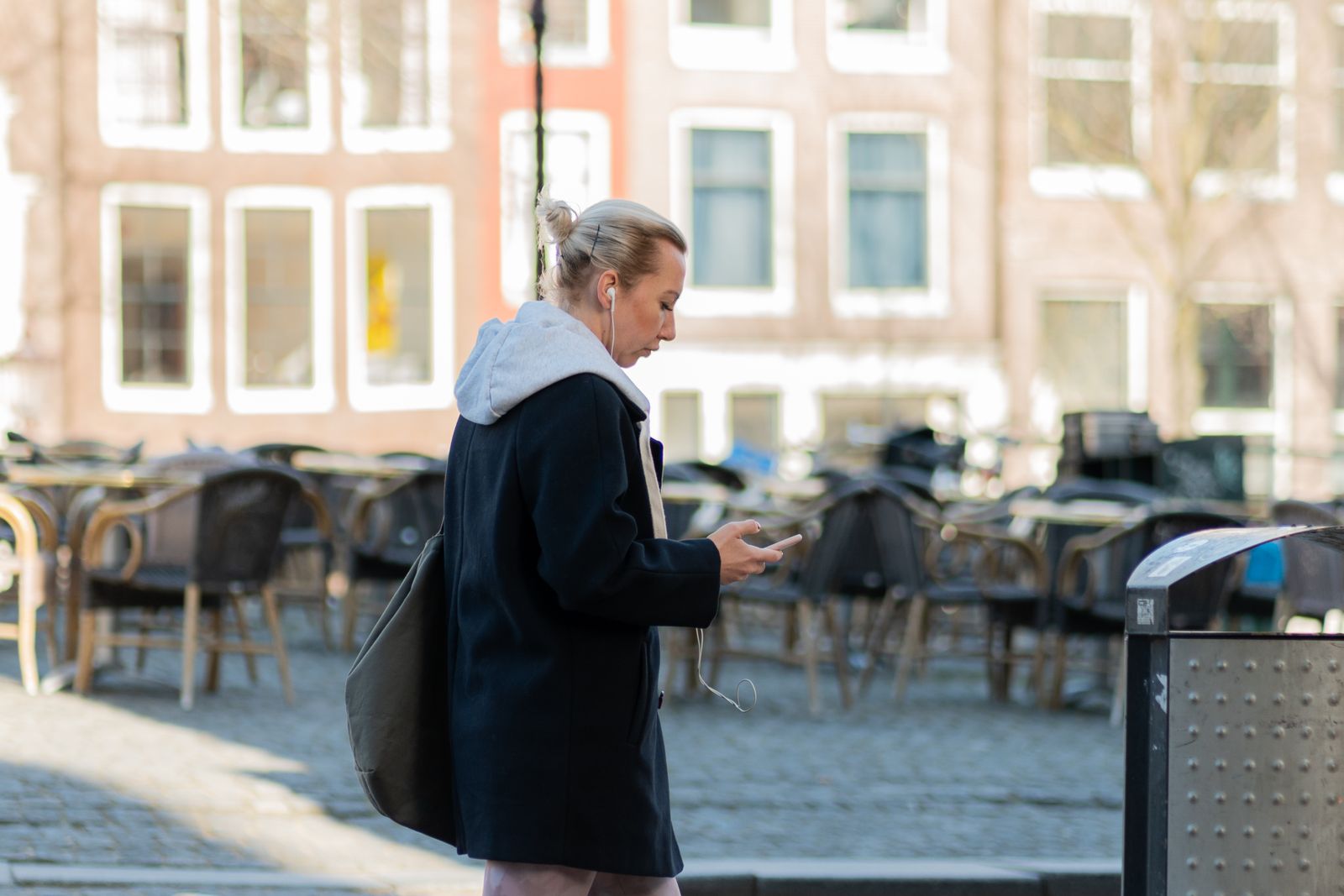 A woman searching on her phone in a city square lined with cafes