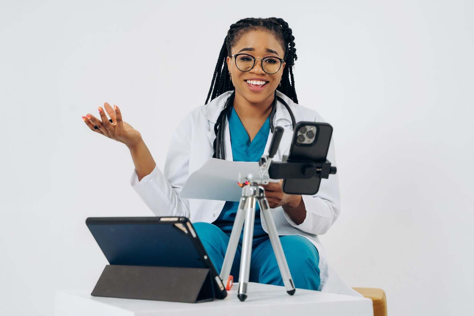 A doctor in scrubs recording a video with a smartphone on a tripod