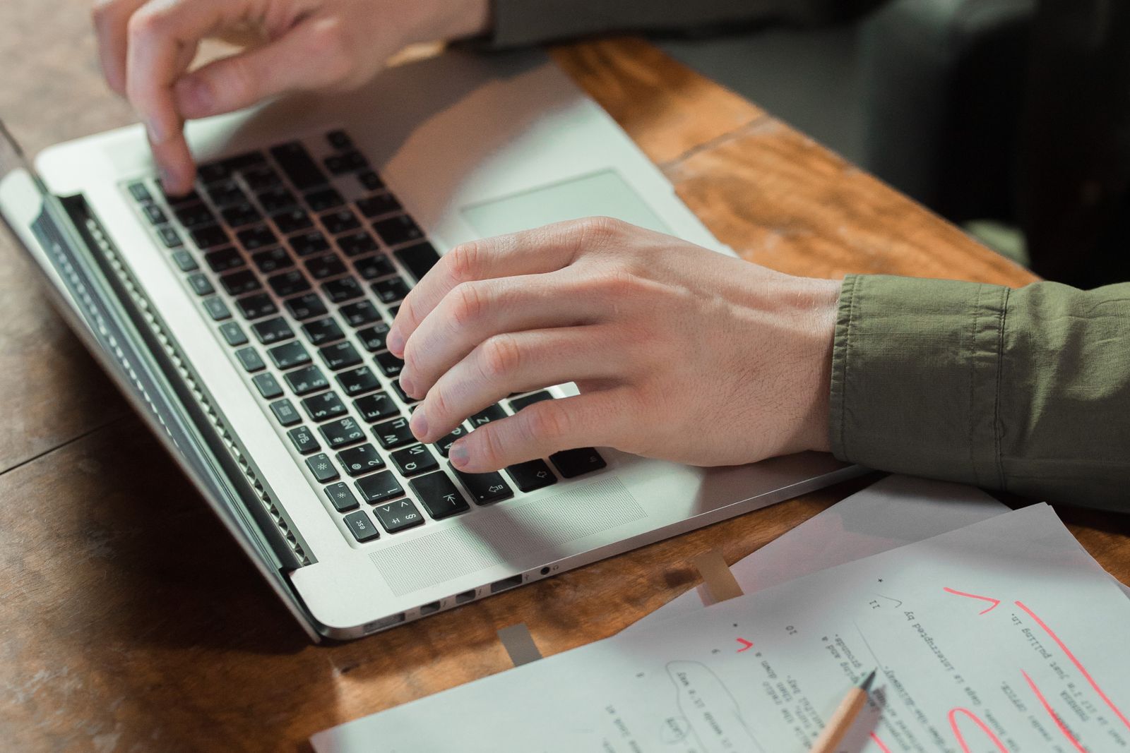 A writer typing with handwritten notes beside the laptop