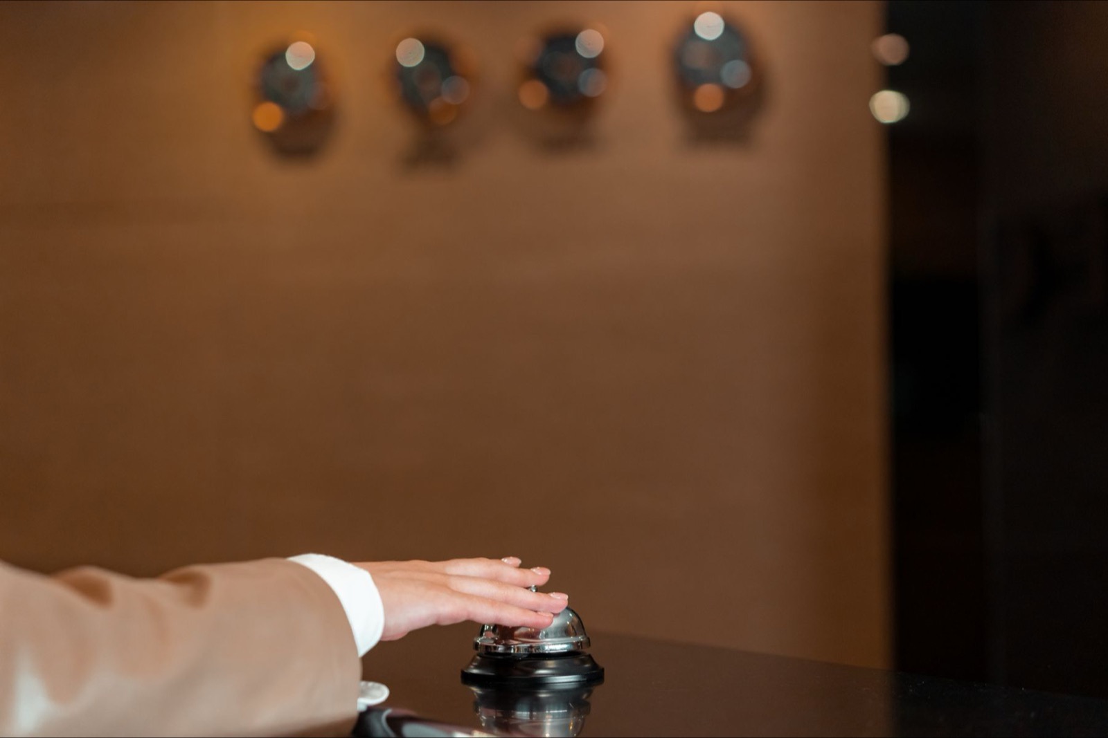 A hand pressing a service bell on a reception desk