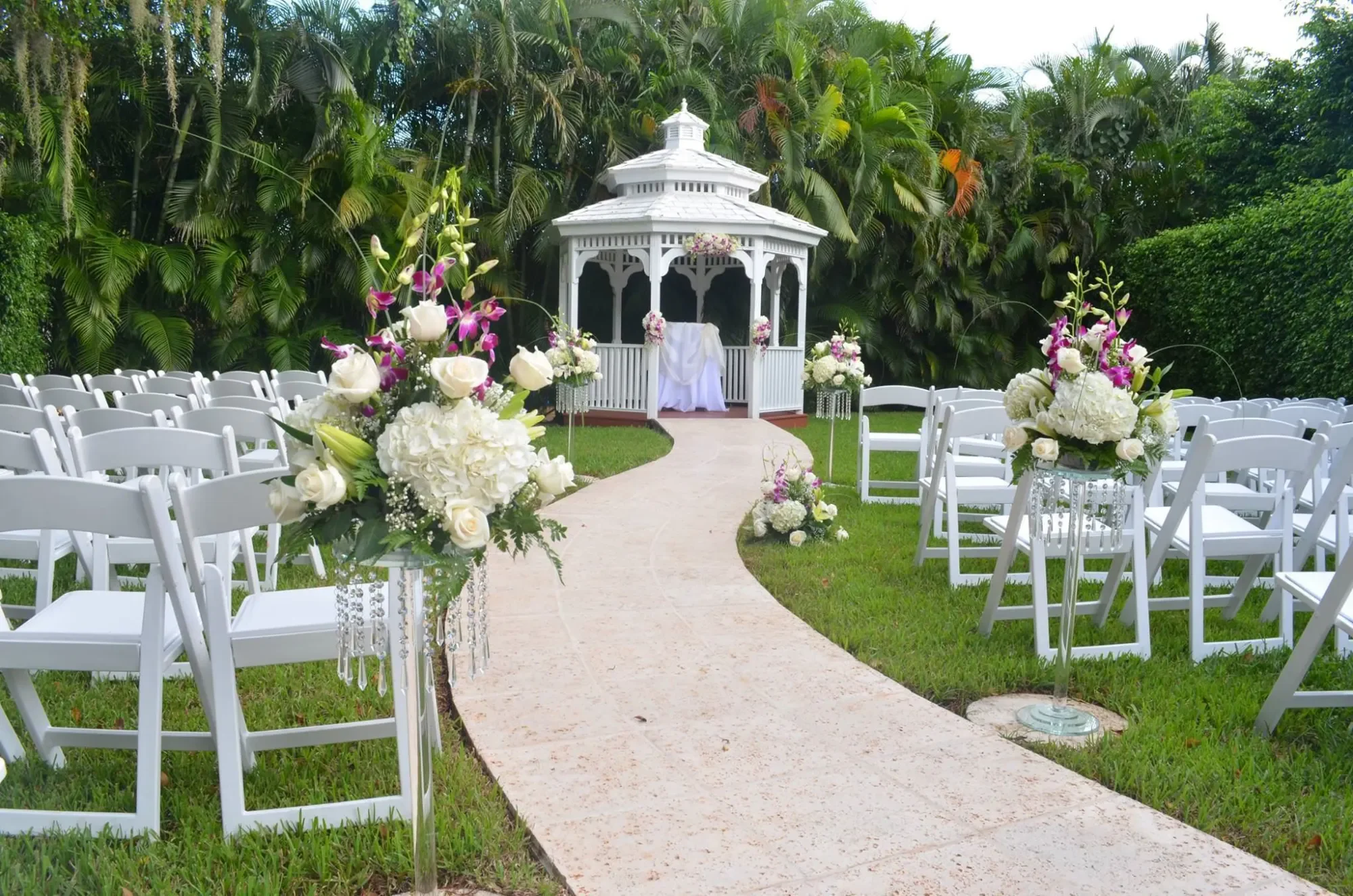 Grand Salon's garden gazebo set for a wedding ceremony, with white chairs and flower-lined aisle
